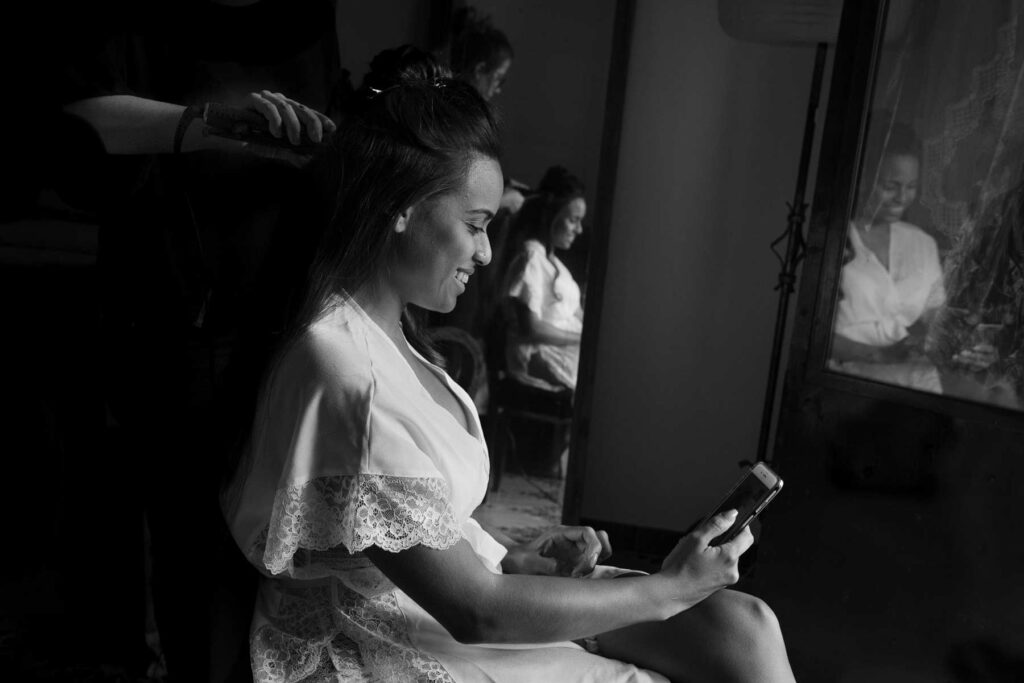 la novia peinándose y sonriendo mientras está mirando el móvil